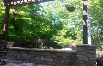 a flagstone porch with a stone wall and wooden pergola