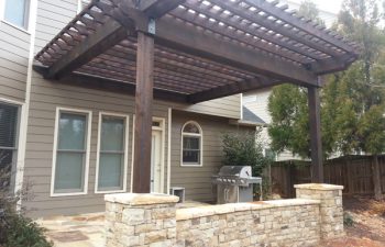 a flagstone porch with a stone wall and wooden pergola